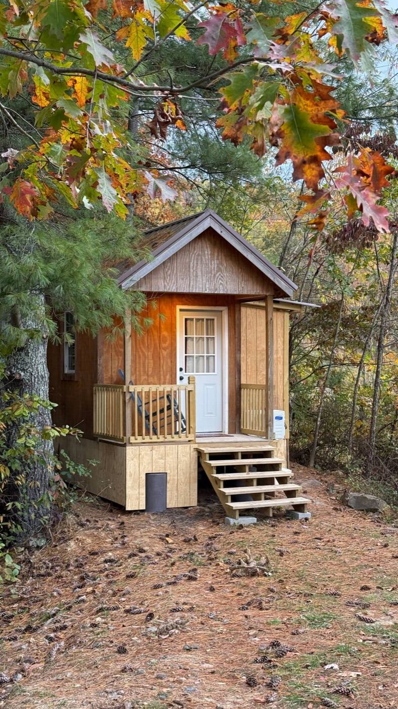 Acorn Cabin, a tiny wood cabin with a small front porch, surrounded by fall trees
