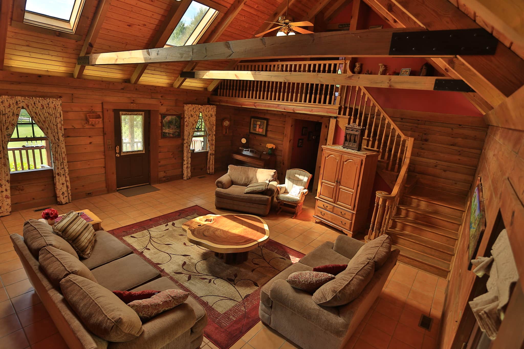 The great room at Maple Fork Lodge: log walls, skylights, exposed beams, and the staircase up to the loft