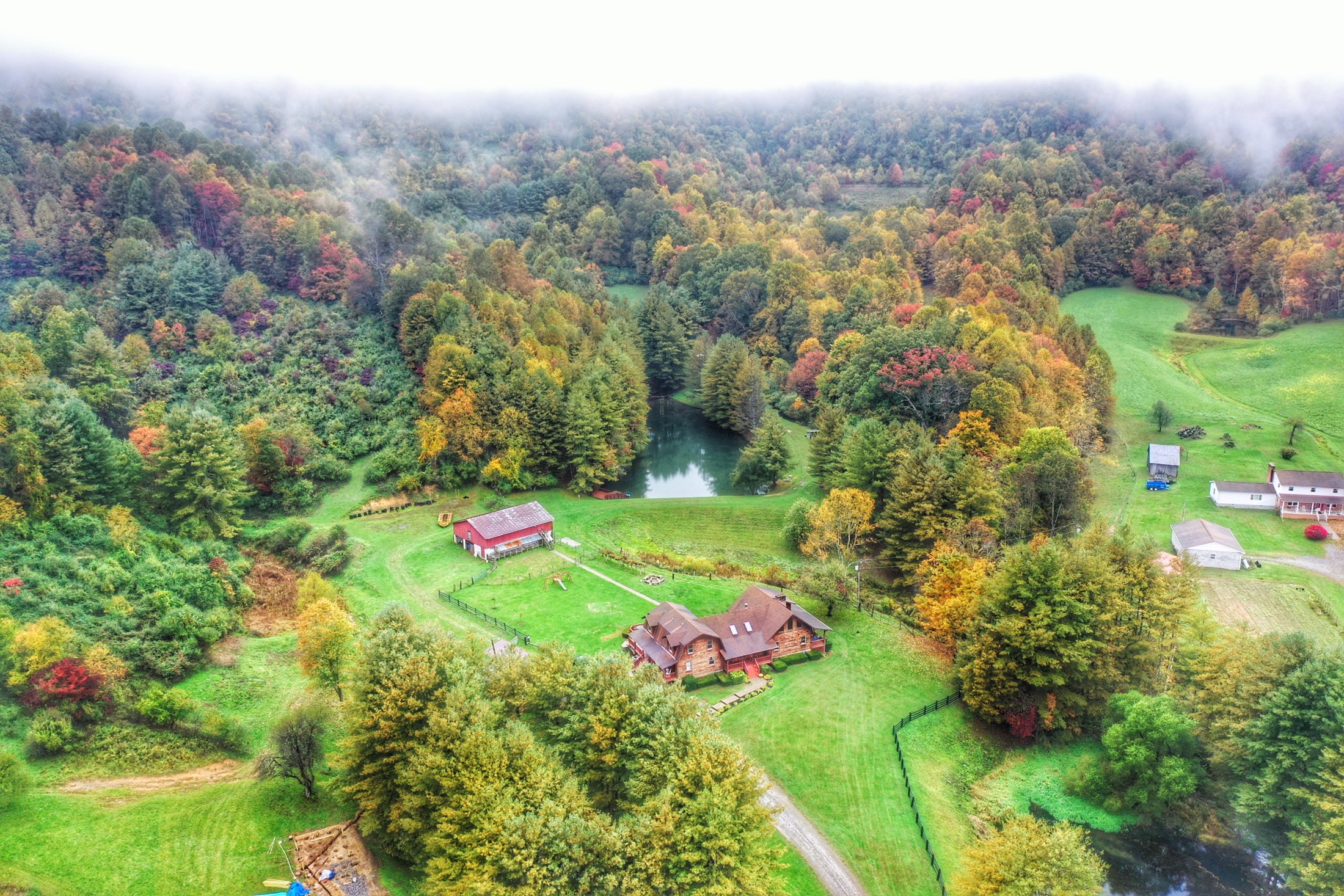 Aerial view of Maple Fork Lodge in autumn: the log lodge, red barn, pond, and surrounding West Virginia hills in fall color