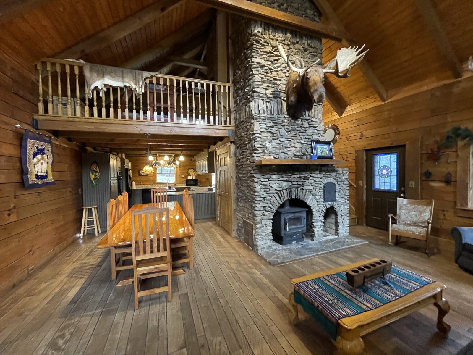 The two-story stone fireplace, dining table, open kitchen, and loft inside the lodge