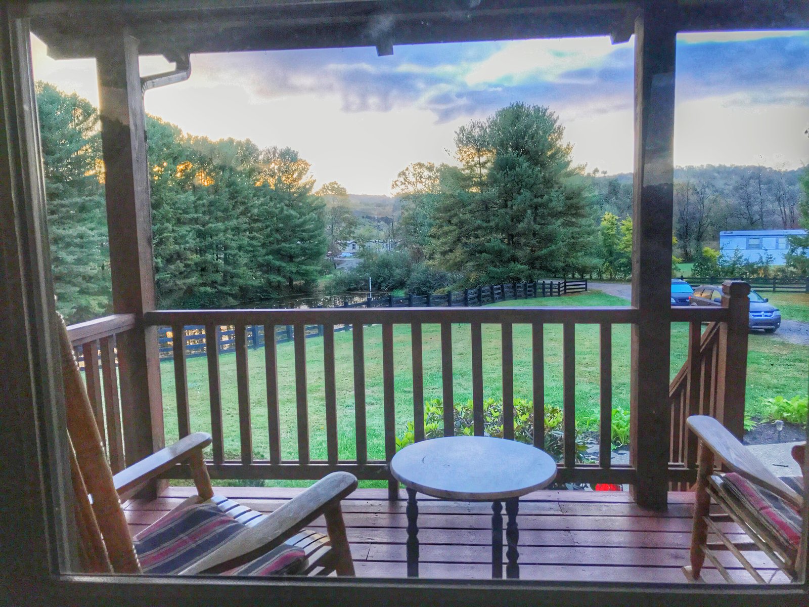 The covered porch with rocking chairs looking out over the pond, pasture, and hills at sunset
